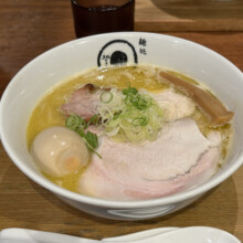 Bowl of ramen topped with sliced pork, a soft-boiled egg, and scallions, served with iced tea