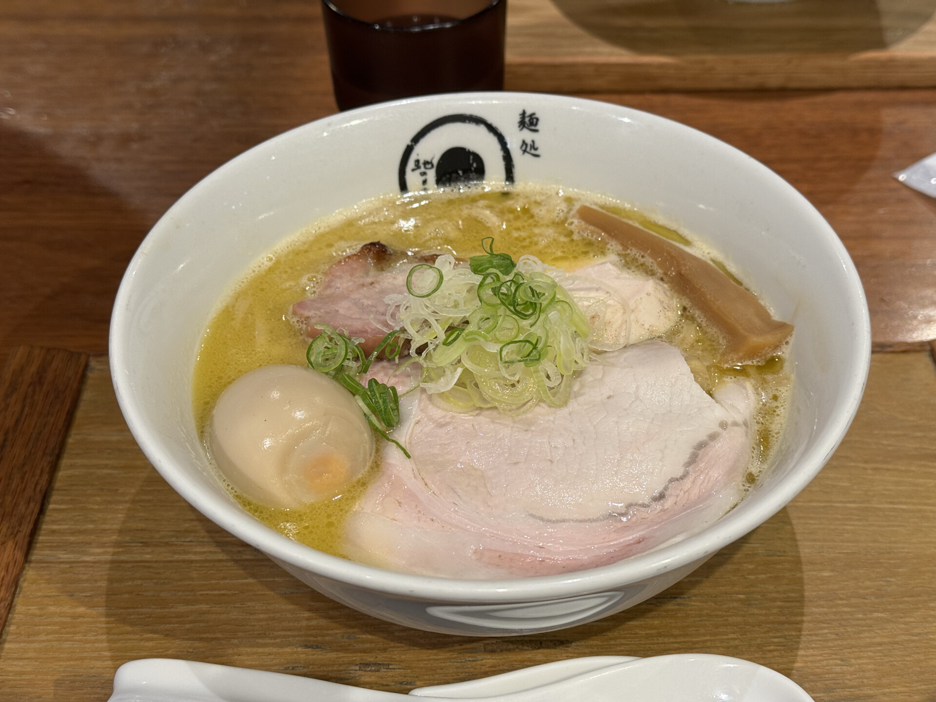 Bowl of ramen topped with sliced pork, a soft-boiled egg, and scallions, served with iced tea