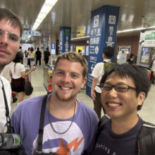 Three visitors smiling for a selfie inside a busy Kyoto subway station