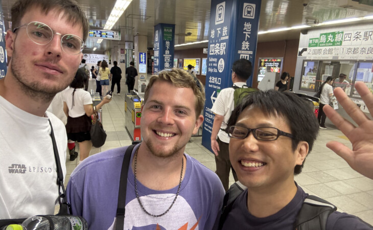 Three visitors smiling for a selfie inside a busy Kyoto subway station
