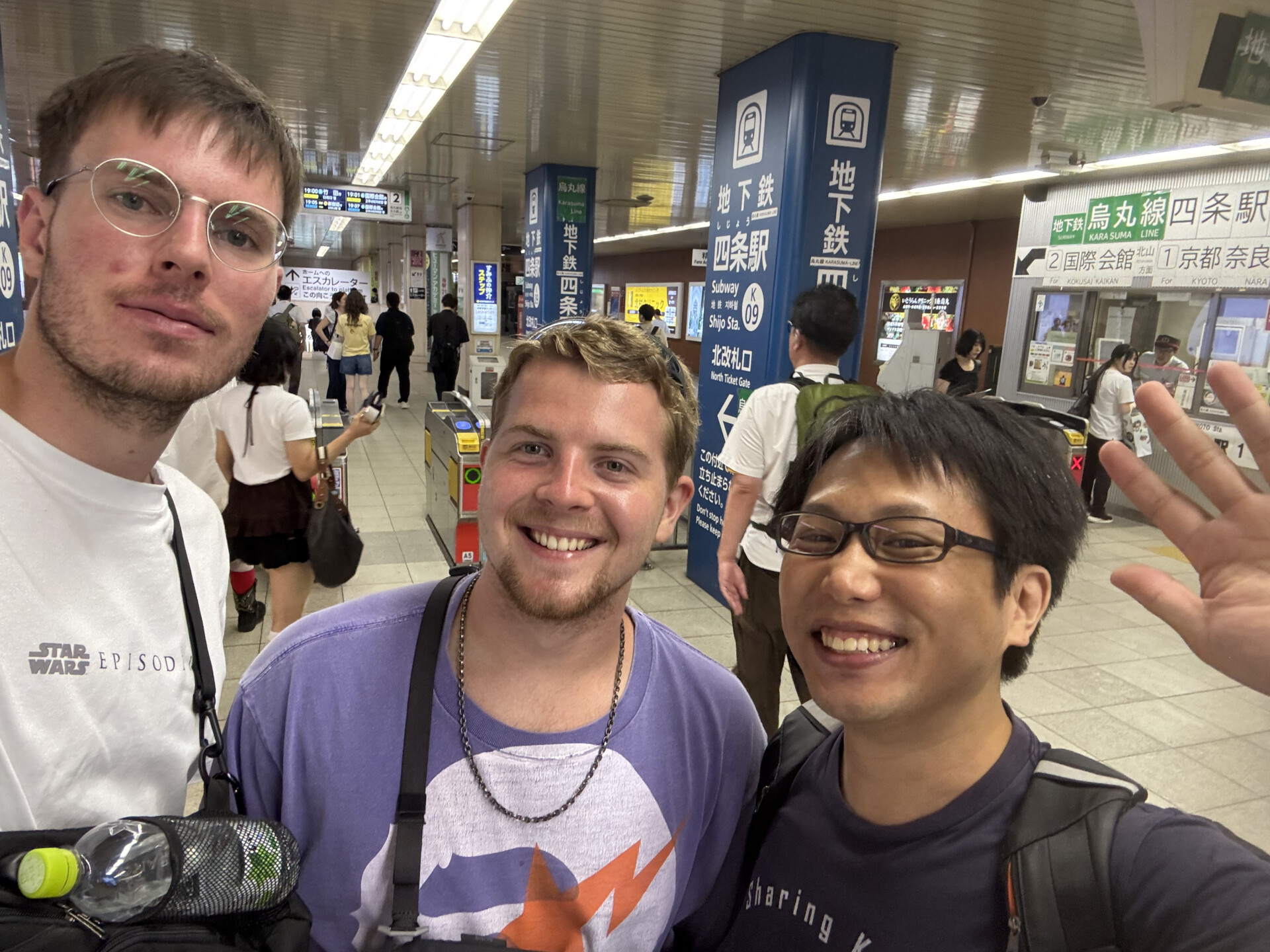Three visitors smiling for a selfie inside a busy Kyoto subway station